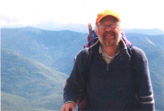 A man in climbing gear in front of a mountain, smiling for the camera