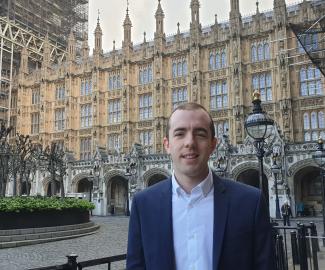A man standing in front of the House of Parliament and smiling for the camera
