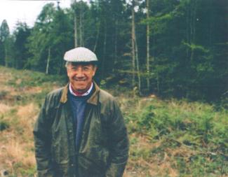 A man standing in front of a woodland, looking at the camera and smiling