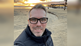 A man looking at the camera with a beach setting