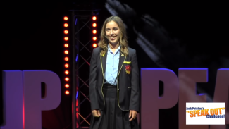 A teenage girl in a school uniform with a microphone smiling