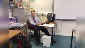 A man sitting at a desk in a classroom, smiling for the camera