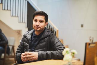 A man looking at the camera and smiling, while holding a coffee cup
