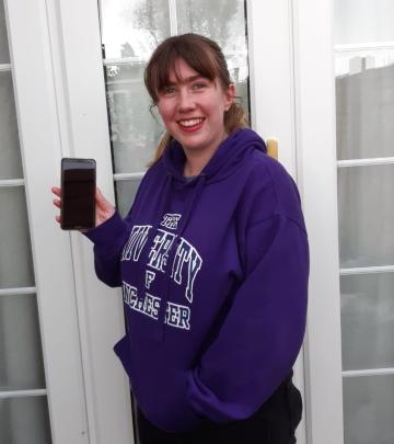 A young woman holding up a smartphone and smiling