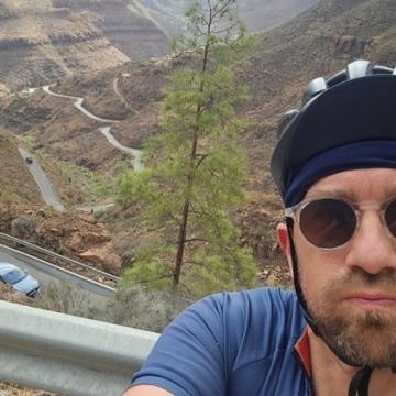 A man in cycling gear and sunglasses looking at the camera, with a mountain pass behind him