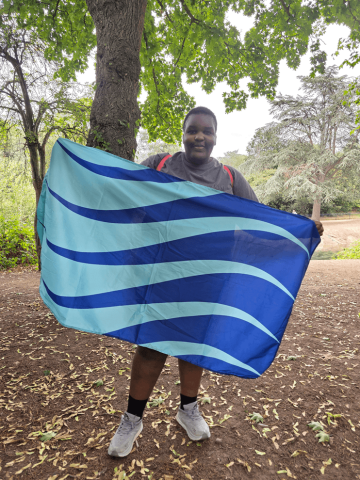 A woman standing in front of trees, holding a flag with both hands
