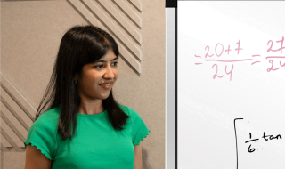 A woman holding a pen and standing beside a whiteboard which has writing on it
