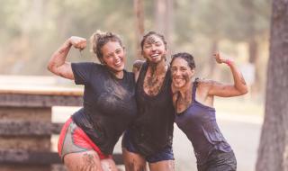 Three women covered in mud posing together after a running event