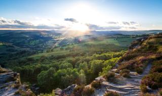 An aerial view of the hills and valleys of the Peak District in Derbyshire, with the sun peaking through clouds