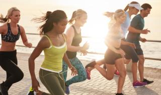 A group of runners, male and female, running next to the coast, with the sun shining behind them