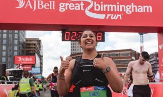 A woman posing at the end of a sponsored run, smiling with her thumbs up