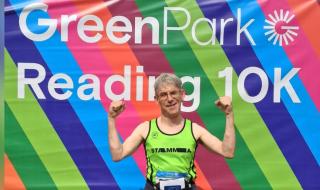 A man in a running vest holding both hands in the air