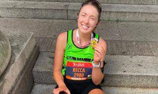 A woman in running gear sitting on a step, holding a medal and smiling