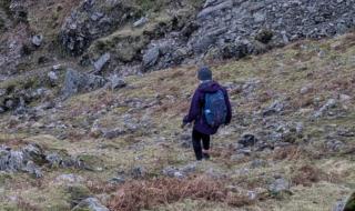 A woman walking down in a hill in the countryside, wearing a backpack.