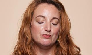 A woman with her eyes closed, trying to talk.