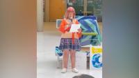 A woman standing with a microphone in her hand, looking at a sheet of paper she's holding