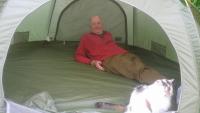 A man lying inside a tent, with a cat in front of him
