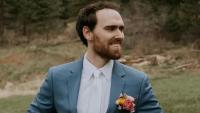 A man in a wedding suit looking to the right and smiling