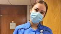A nurse wearing a facemask looking at the camera and tilting her head
