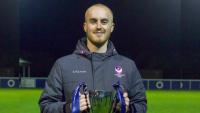 A man standing on a football pitch, holding a trophy and smiling