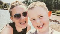 A woman wearing sunglasses standing next to her young son, in front of a lake. Both are smiling