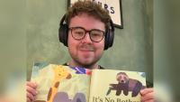 A man wearing headphones and holding up a children's book