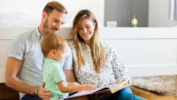 A mother and father sitting with their young son and reading a book