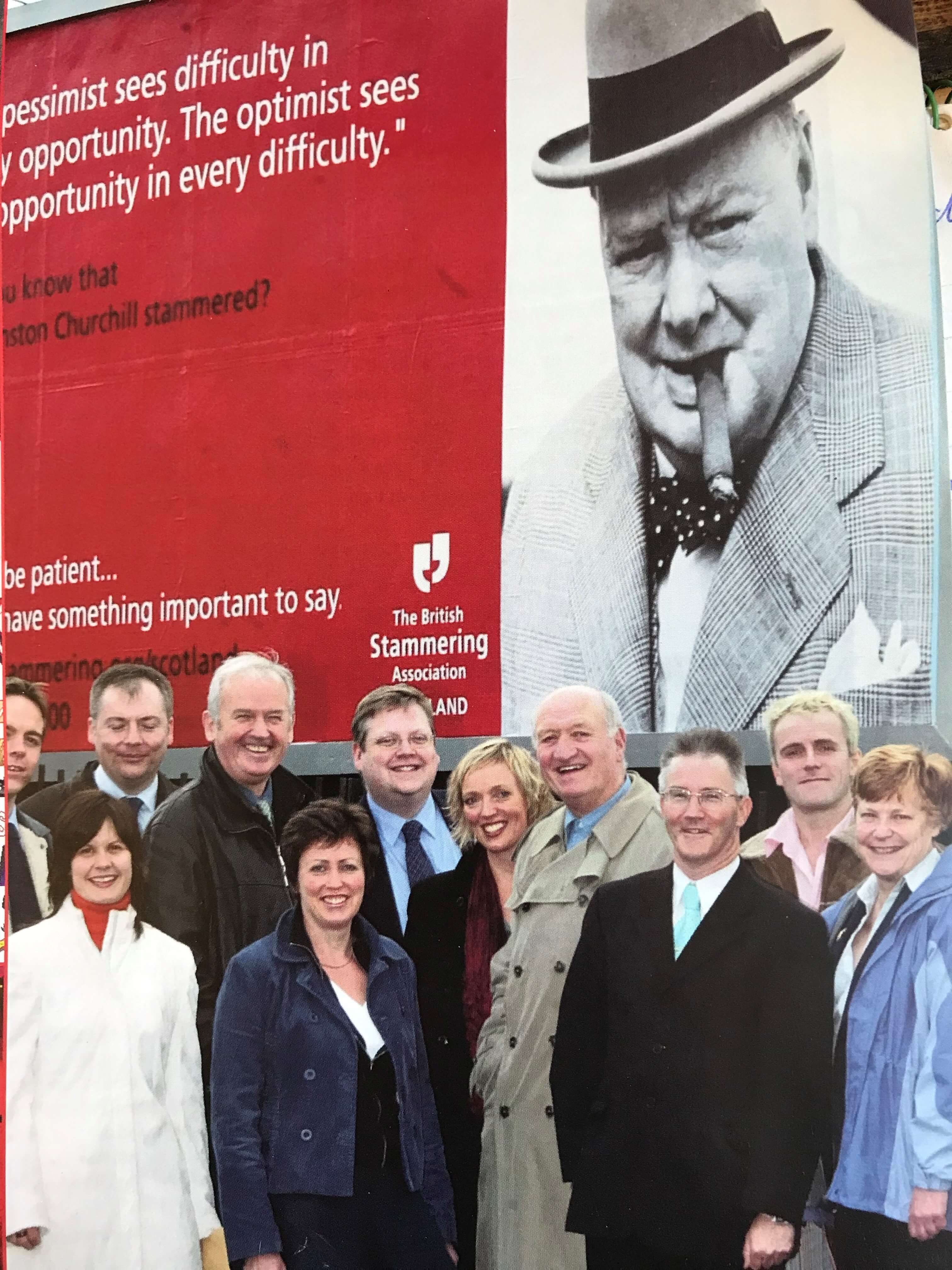 A group of people in front of a billboard poster, looking at the camera