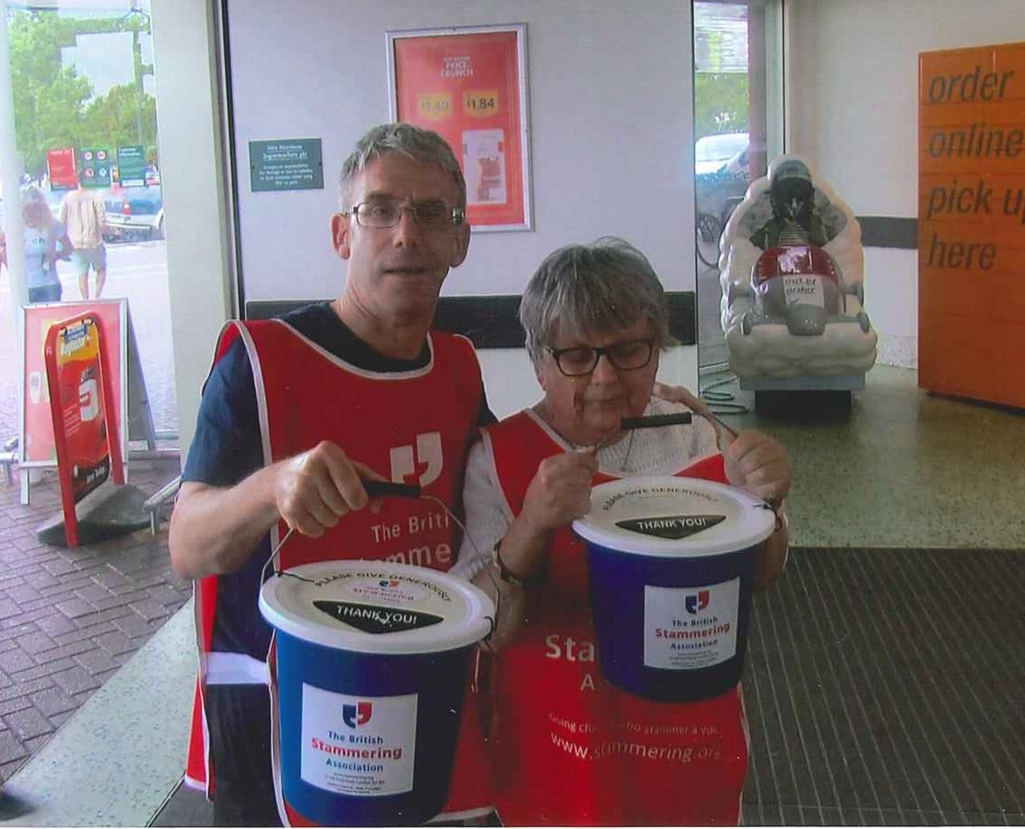 A man and a woman holding charity collection buckets, looking at the camera