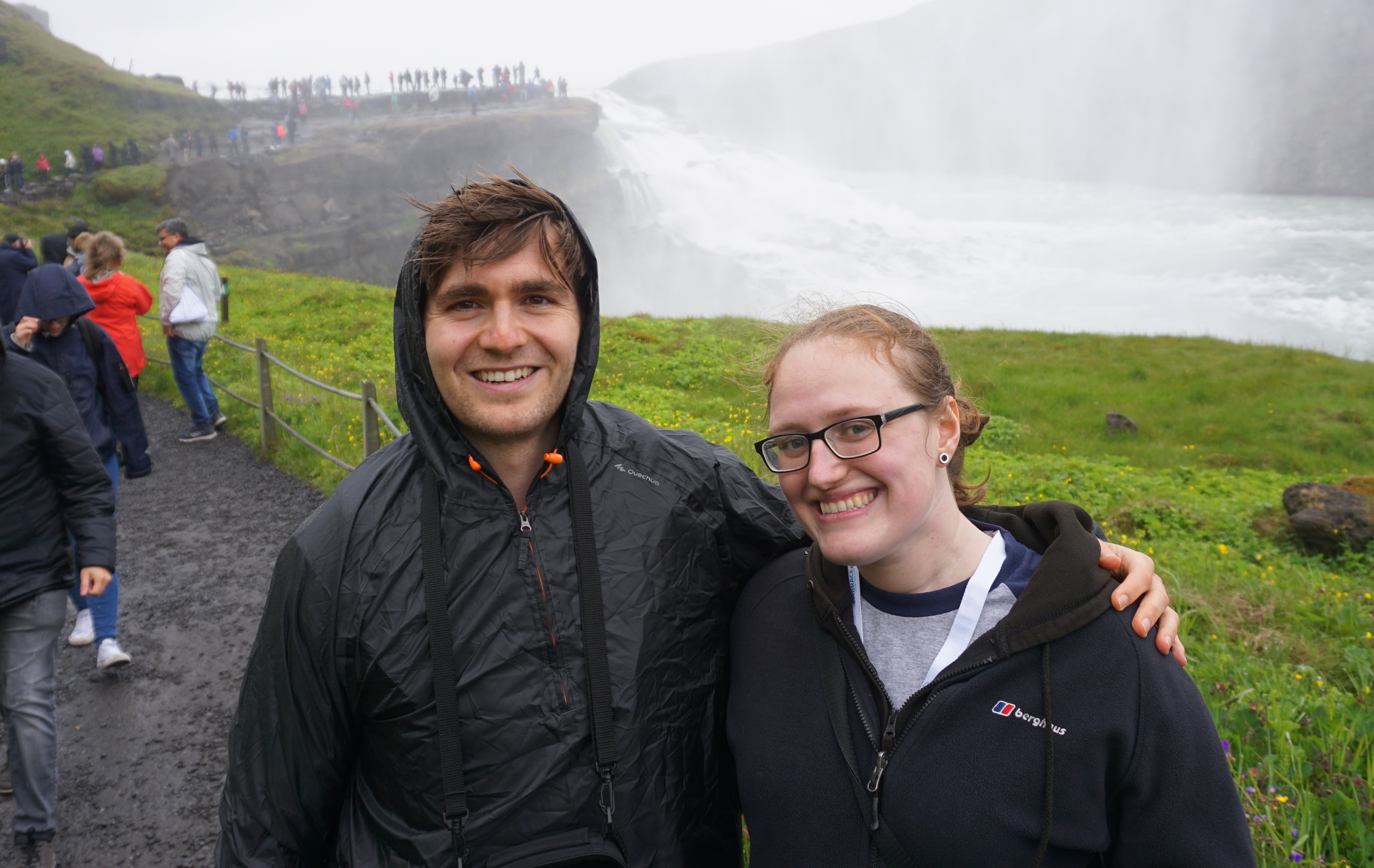 A man and a woman looking at the camera in front of a waterfall