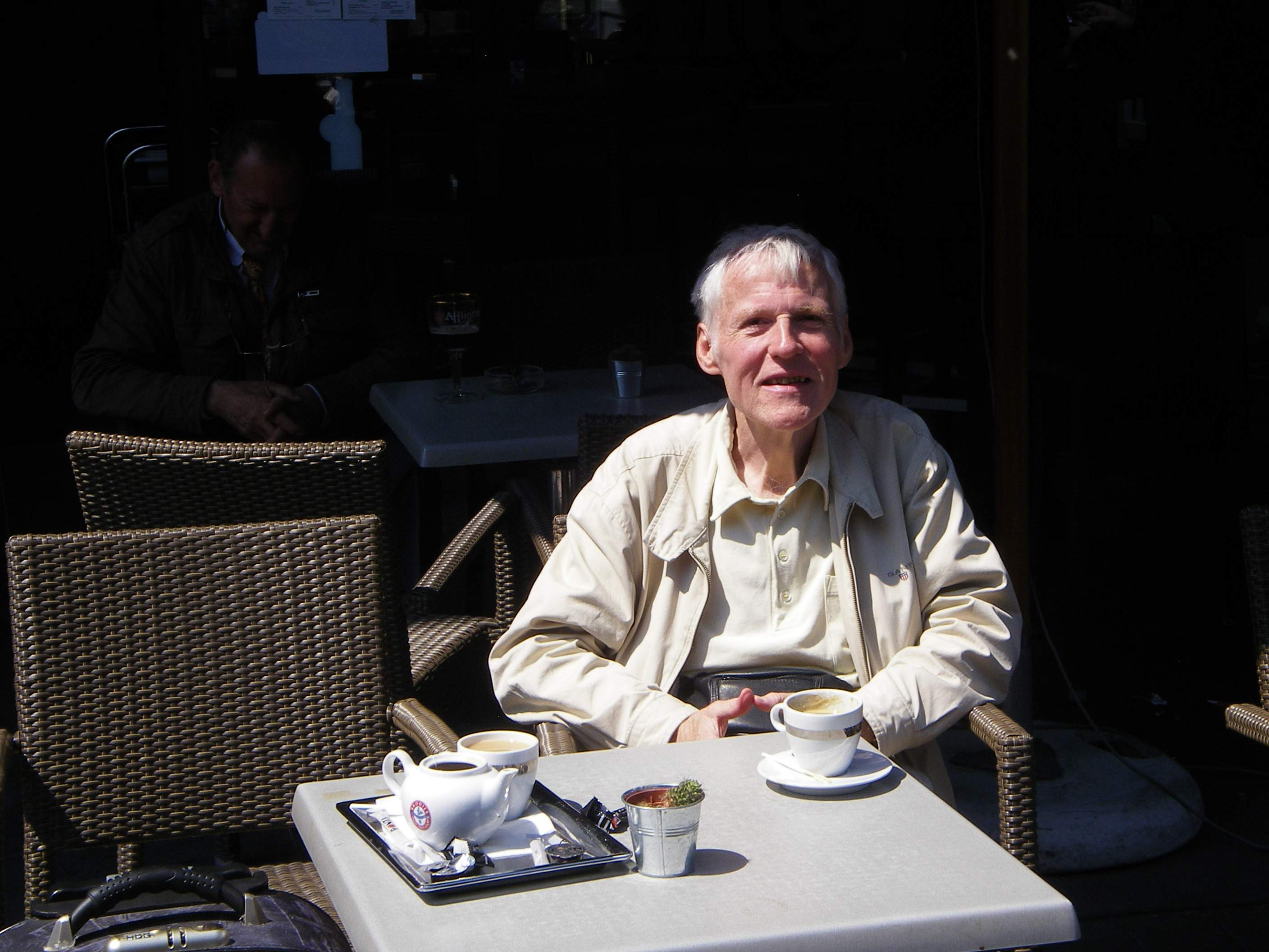 An elderly man sitting at a cafe table outdoors.
