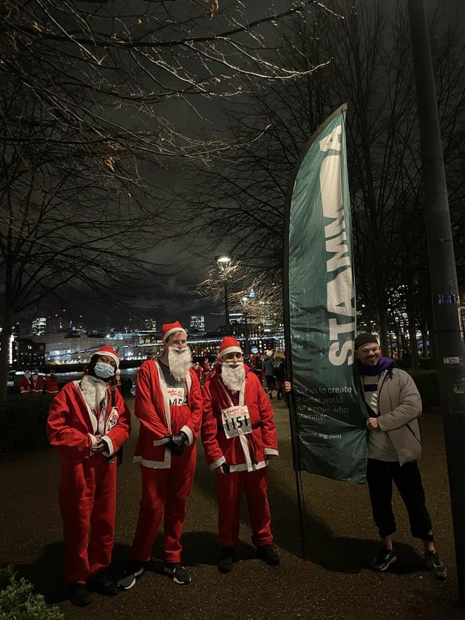 People dressed as Father Christmas next to a STAMMA banner