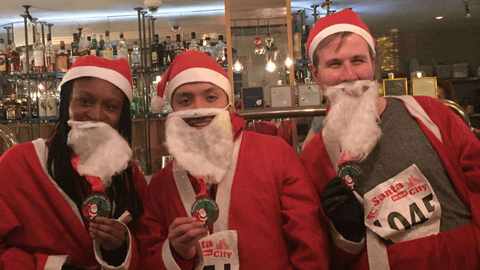Three people dressed as Father Christmas looking at the camera and smiling