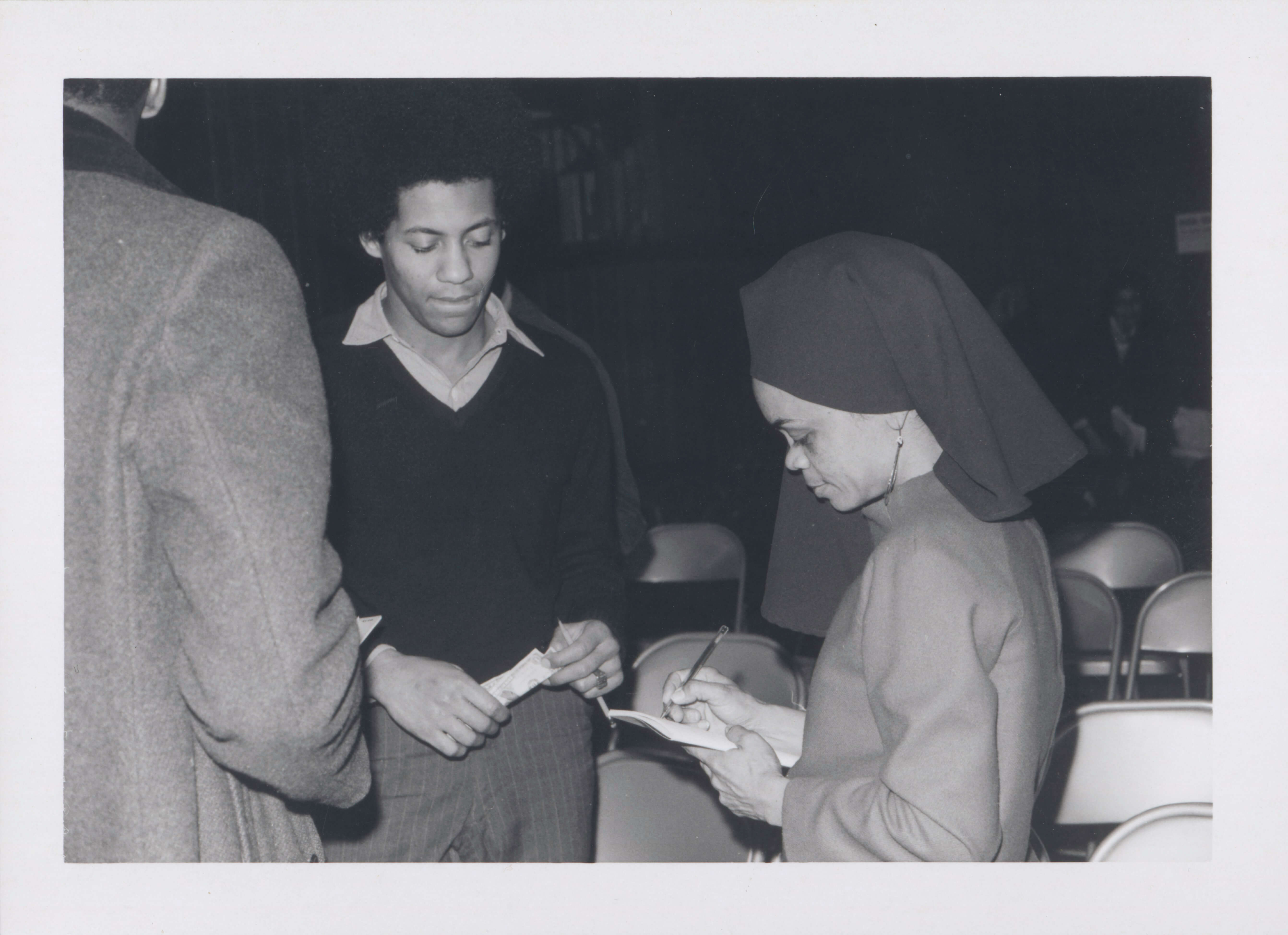 Black and white photograph of a woman signing an autograph for a man who is standing beside