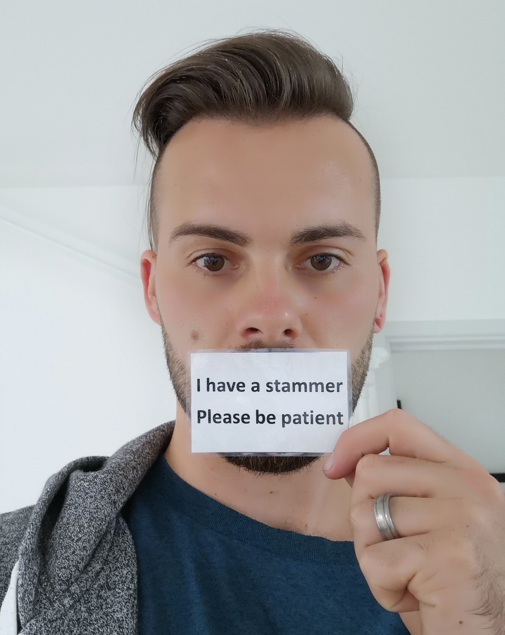 A man holding a card in front of his mouth that reads 'I have a stammer. Please be patient'