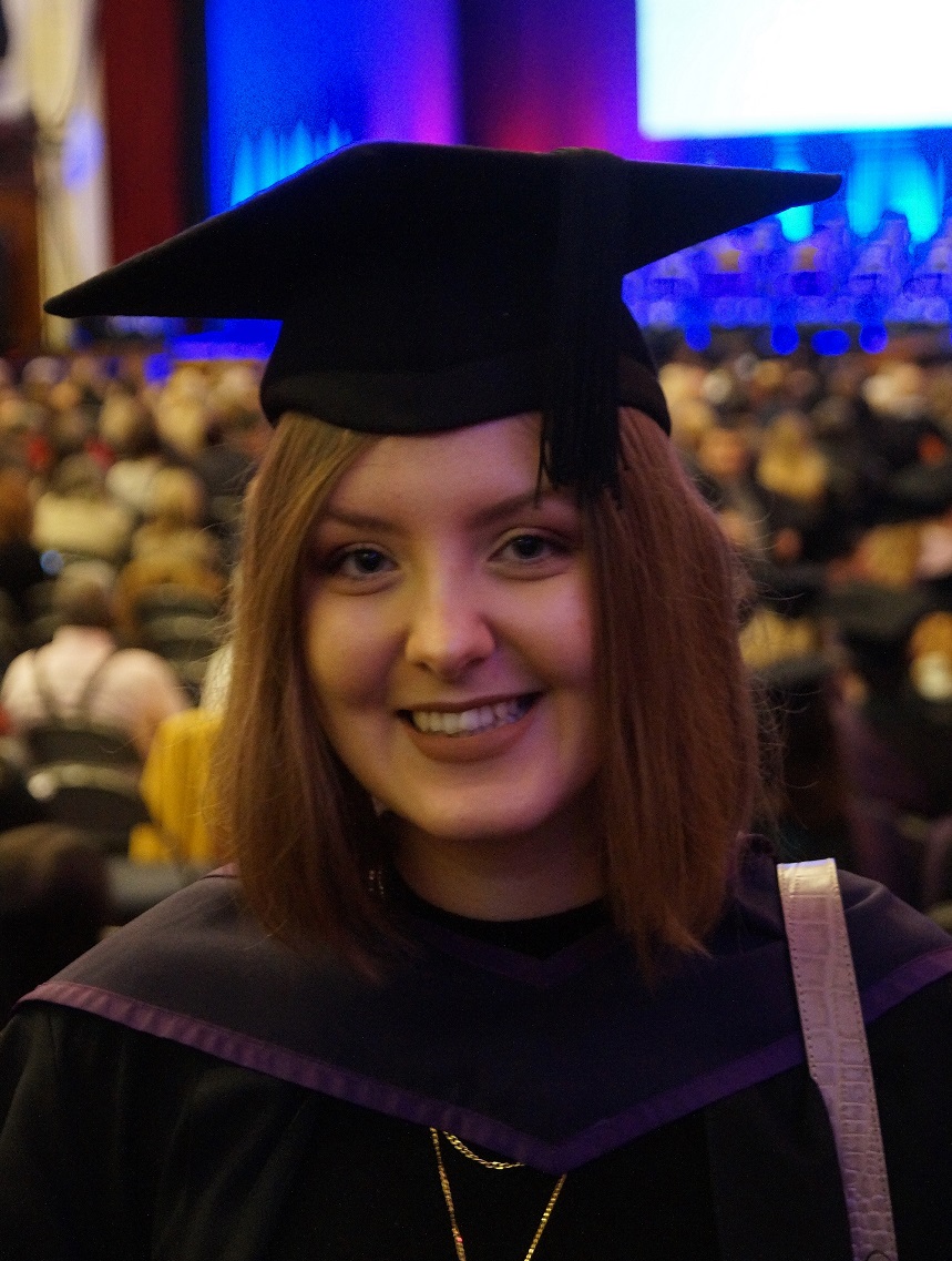 A woman in a graduation gown looking at the camera and smiling
