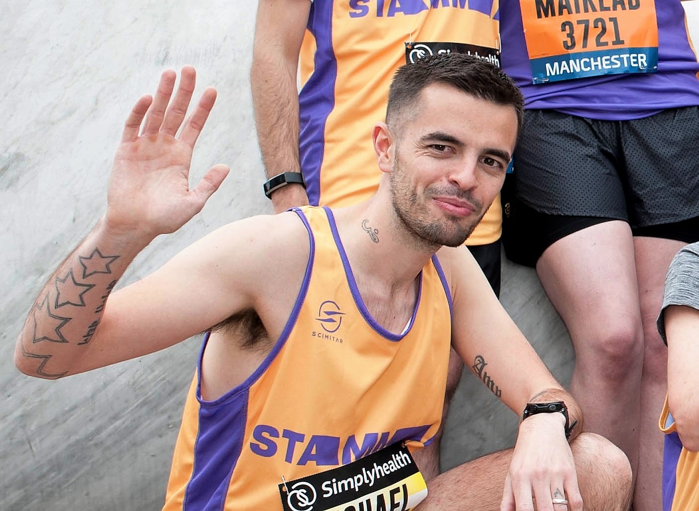 A man in a running vest looking at the camera and waving