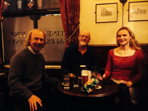 Two men and a woman sitting in a pub, smiling for the camera