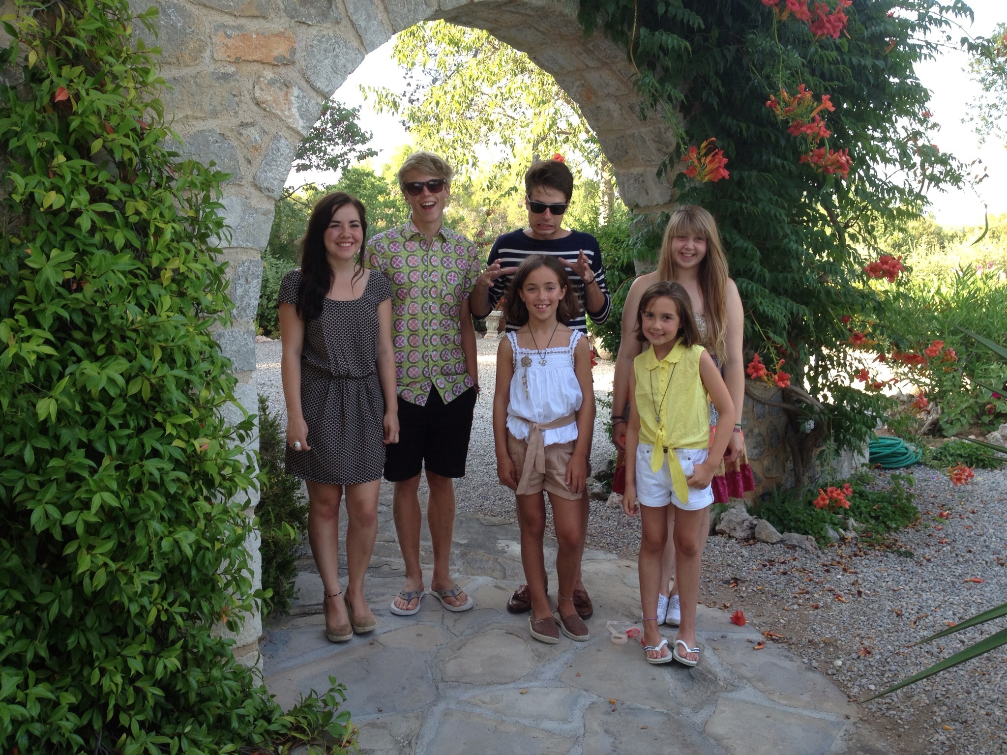 Two teenage boys in sunglasses and a teenage girl standing with three young girls, all smiling